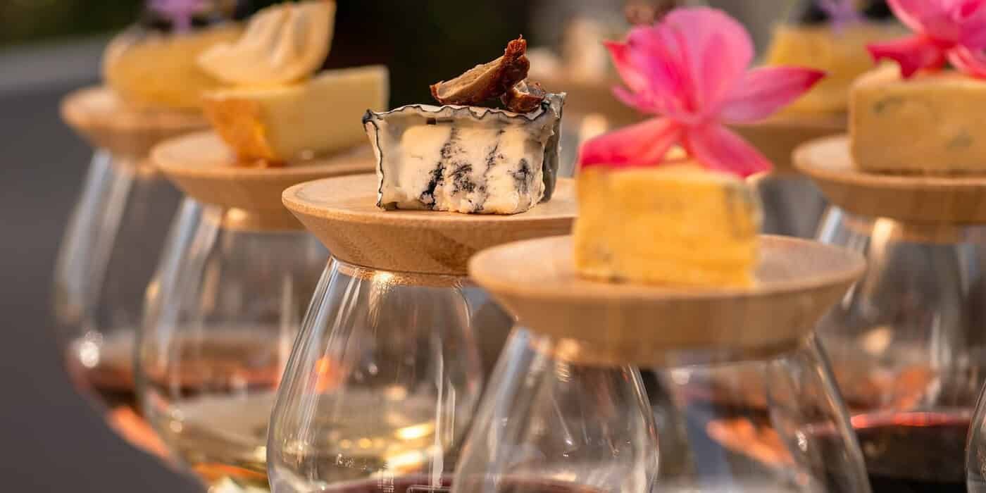 Assorted gourmet cheeses with edible flowers served on wooden pegs at Palm House Boutique Hotel and Spa, perfect for a luxury wine and dine experience.
