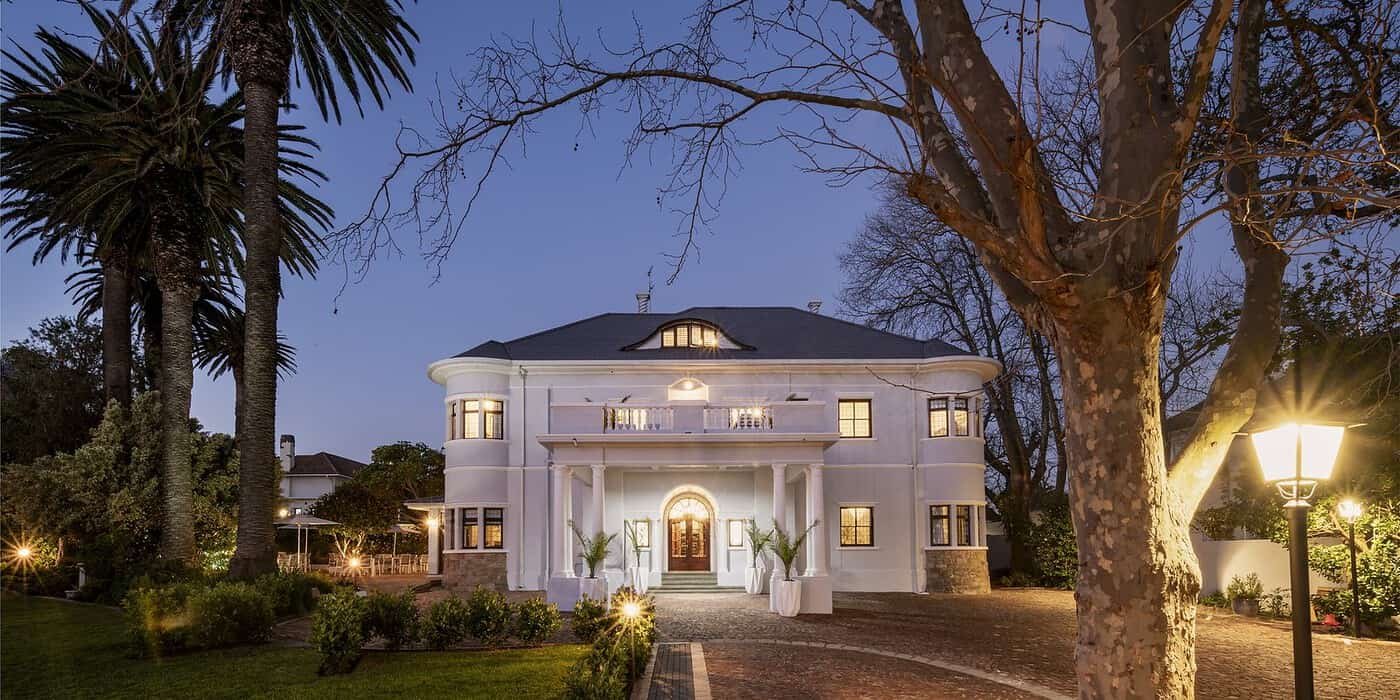 Elegant white boutique hotel with classic architecture surrounded by lush greenery and palm trees in a tranquil, upscale setting.