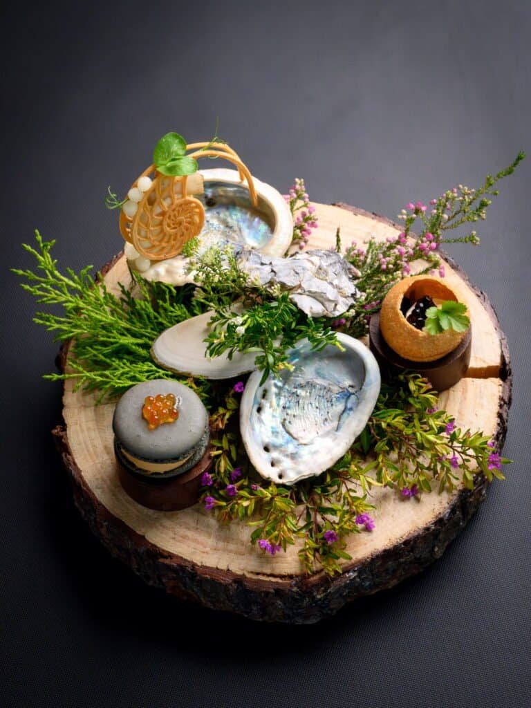 Elegant seafood platter featuring fresh oysters, garnished with herbs and edible flowers, served on a rustic wooden slice at Palm House Boutique Hotel and Spa.