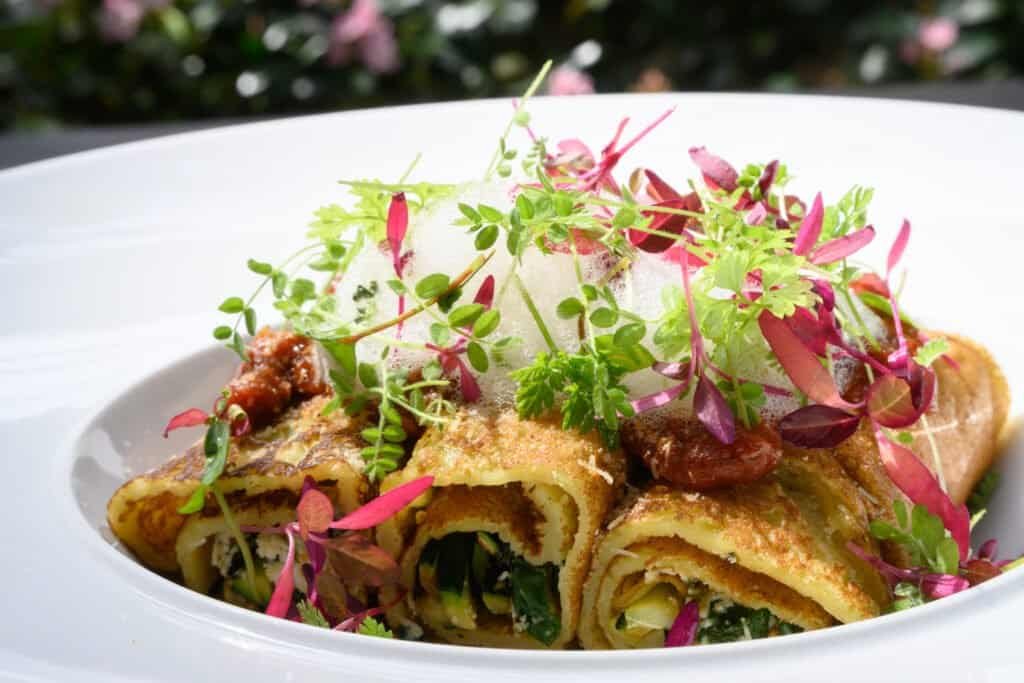 Fresh gourmet dish featuring rolled pancakes topped with microgreens and foam, showcasing elegant presentation at Palm House Boutique Hotel and Spa.