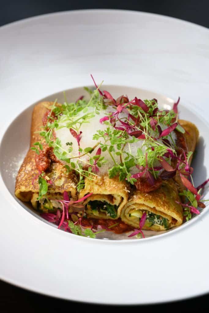 Fresh gourmet vegetable and meat spring roll garnished with microgreens, served on a white plate, highlighting elegant dining at Palm House Boutique Hotel and Spa.