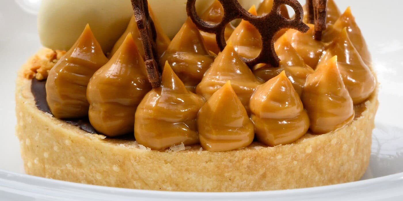 Creamy caramel tart with chocolate decorations, topped with white chocolate curl, served on a white plate at Palm House Boutique Hotel and Spa.